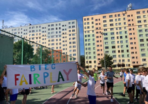 Uczniowie biegnący w strojach sportowych z transparentem Bieg Fair Play